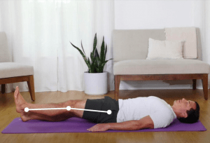 Image shows a man measuring knee extension range of motion. He is lying on a yoga mat on his back with both legs extended, extending the knees so the legs are straight